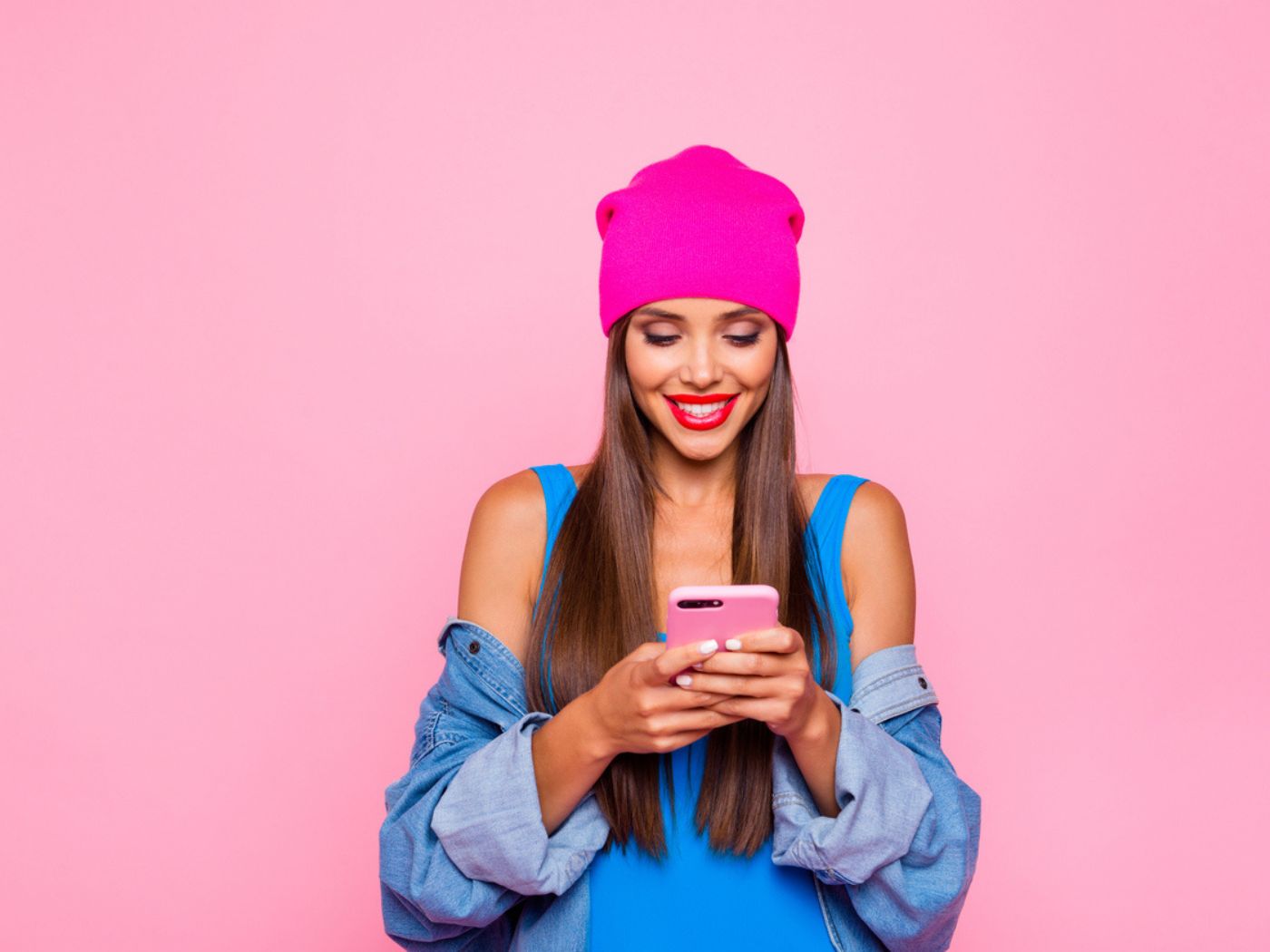 Woman in denim jacket with long hair and a beanie smiling while on her cell phone