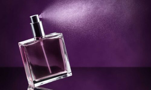 Clear, square fragrance bottle spraying against a purple background