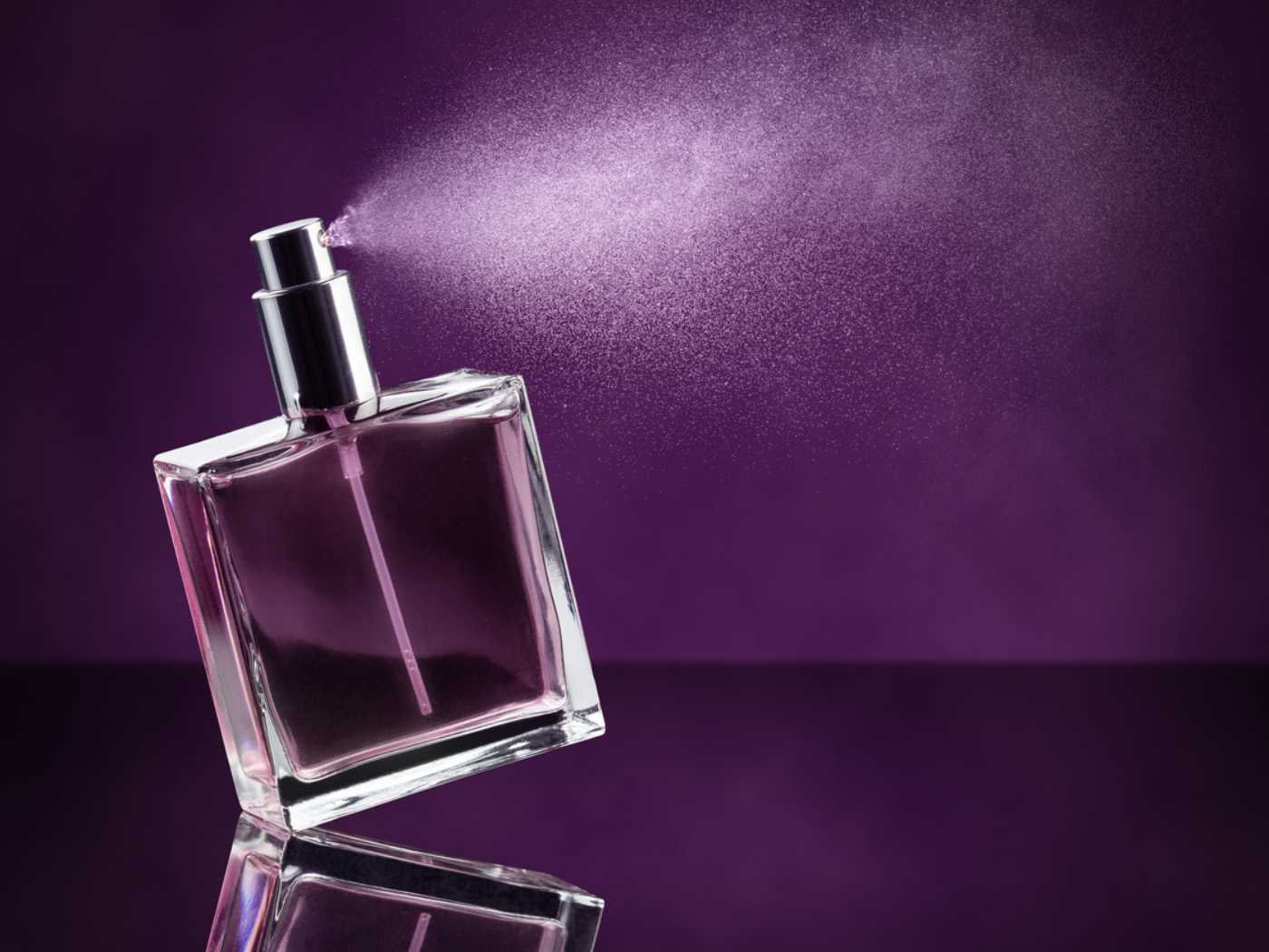 Clear, square fragrance bottle spraying against a purple background