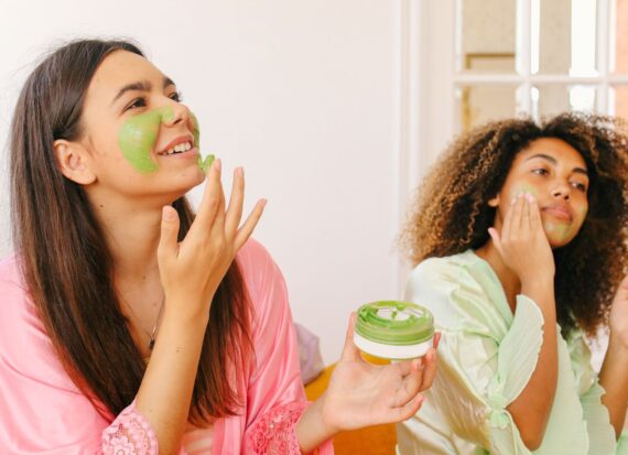 Two women putting a green face mask on their face