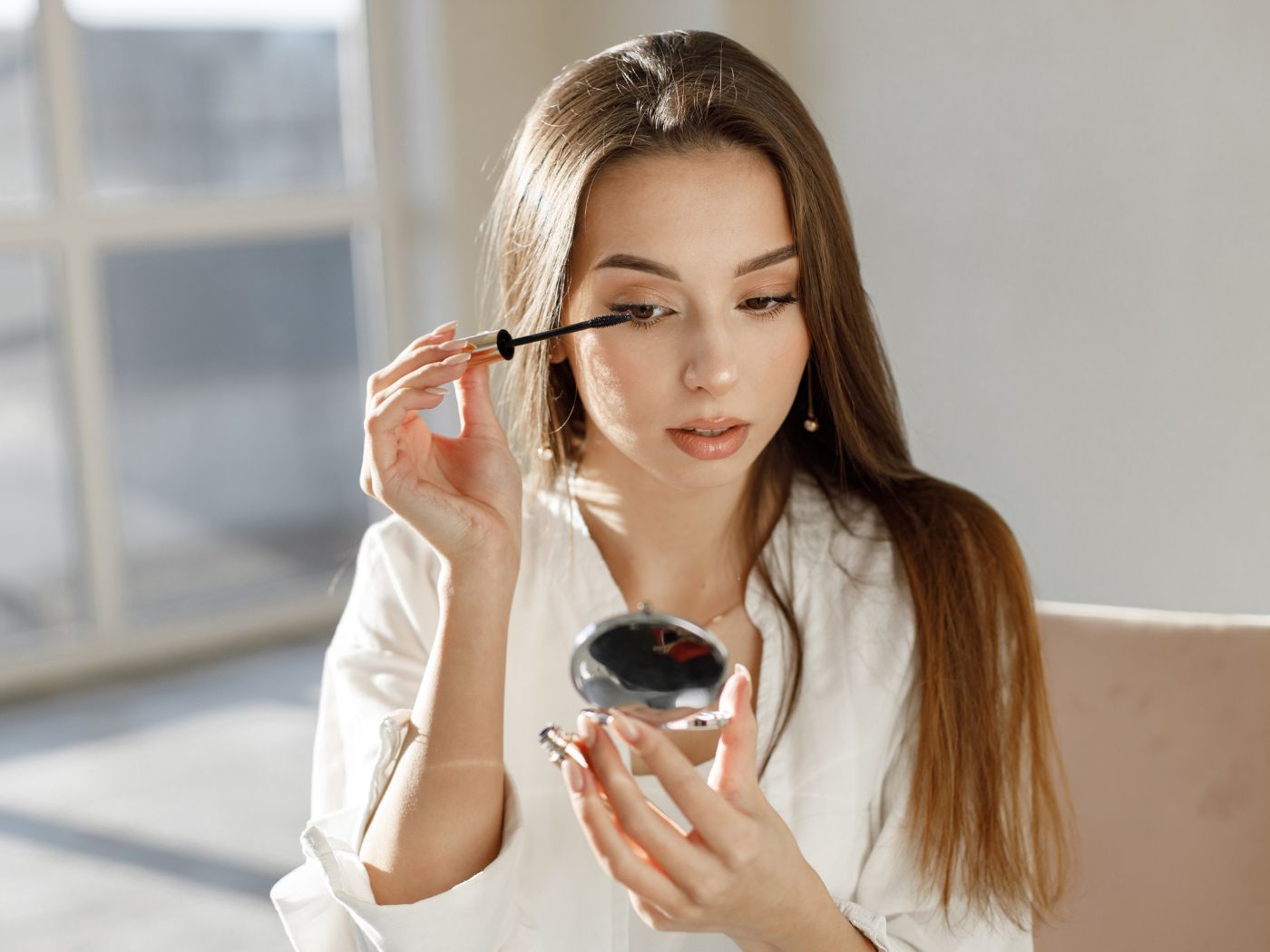 Woman applying mascara using a compact mirror