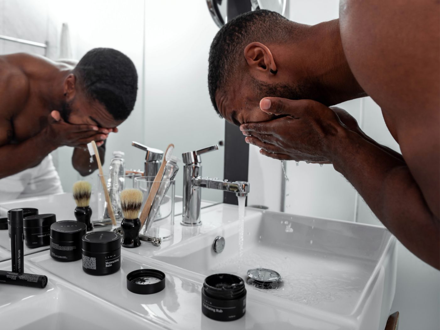 Black man rinsing his face in a bathroom sick during skin care routine