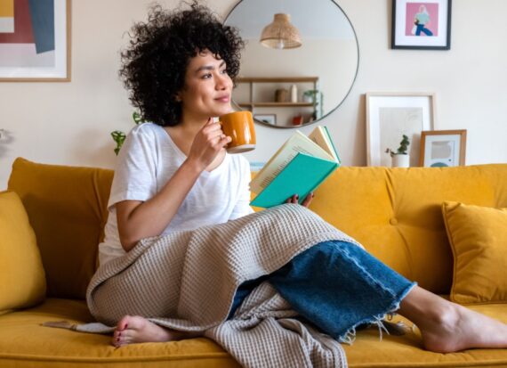 McKinsey’s Top Read Articles For Q1 Can Help You Professionally And Personally Woman on a couch with a book and mug and blanket