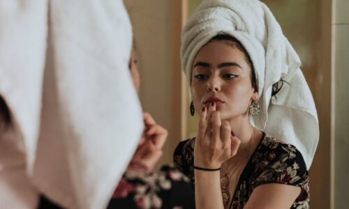 Gen z woman applying lip color in the mirror with a towel on her head