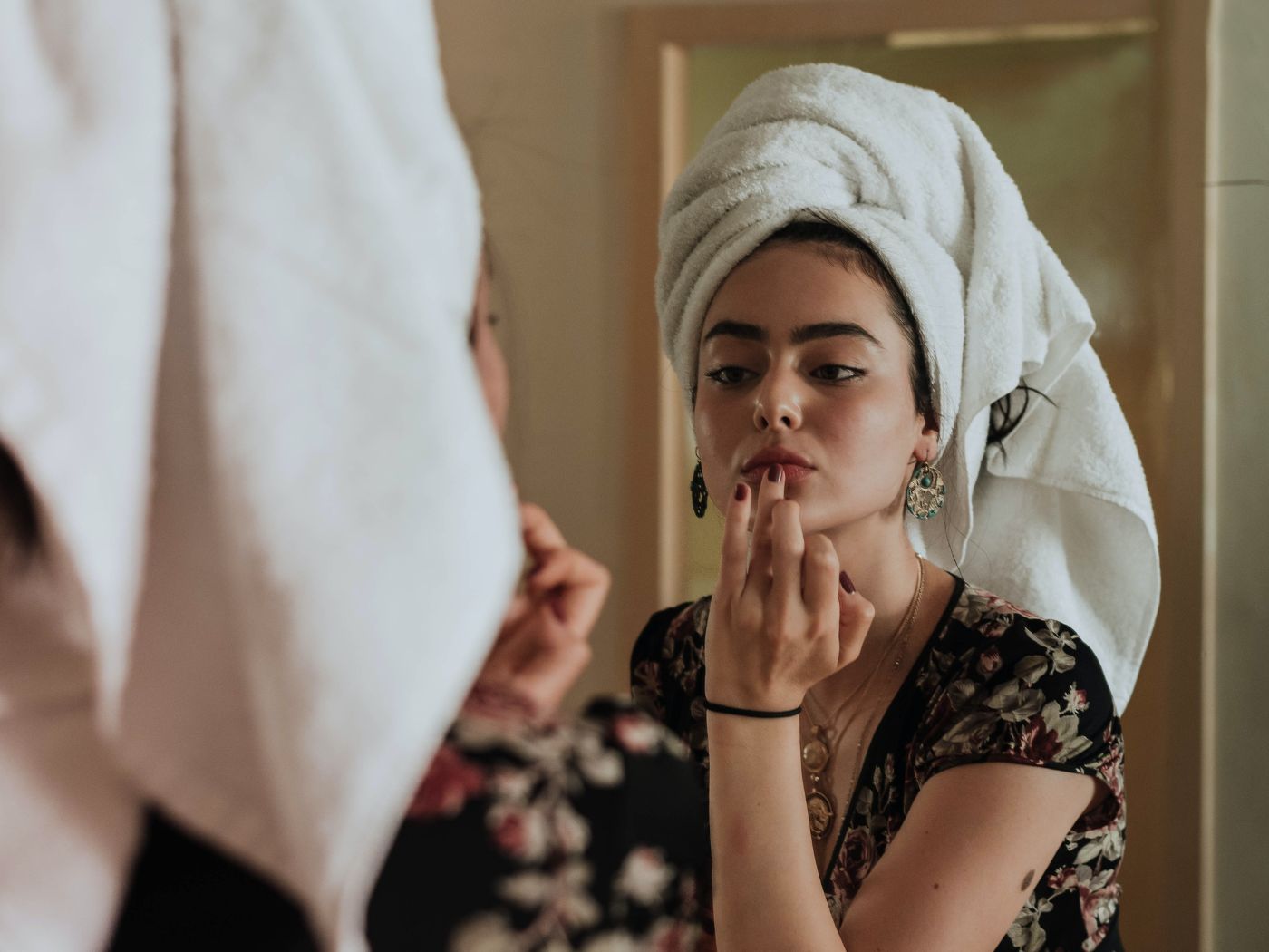 Gen z woman applying lip color in the mirror with a towel on her head
