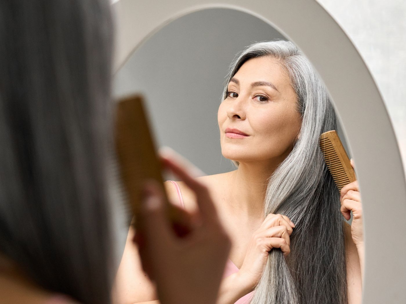 Woman brushing her long, gray hair in the mirror