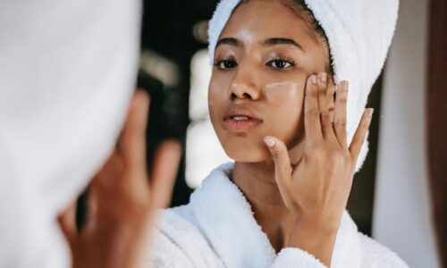 Woman in a towel hair wrap and robe putting moisturizer on her cheek