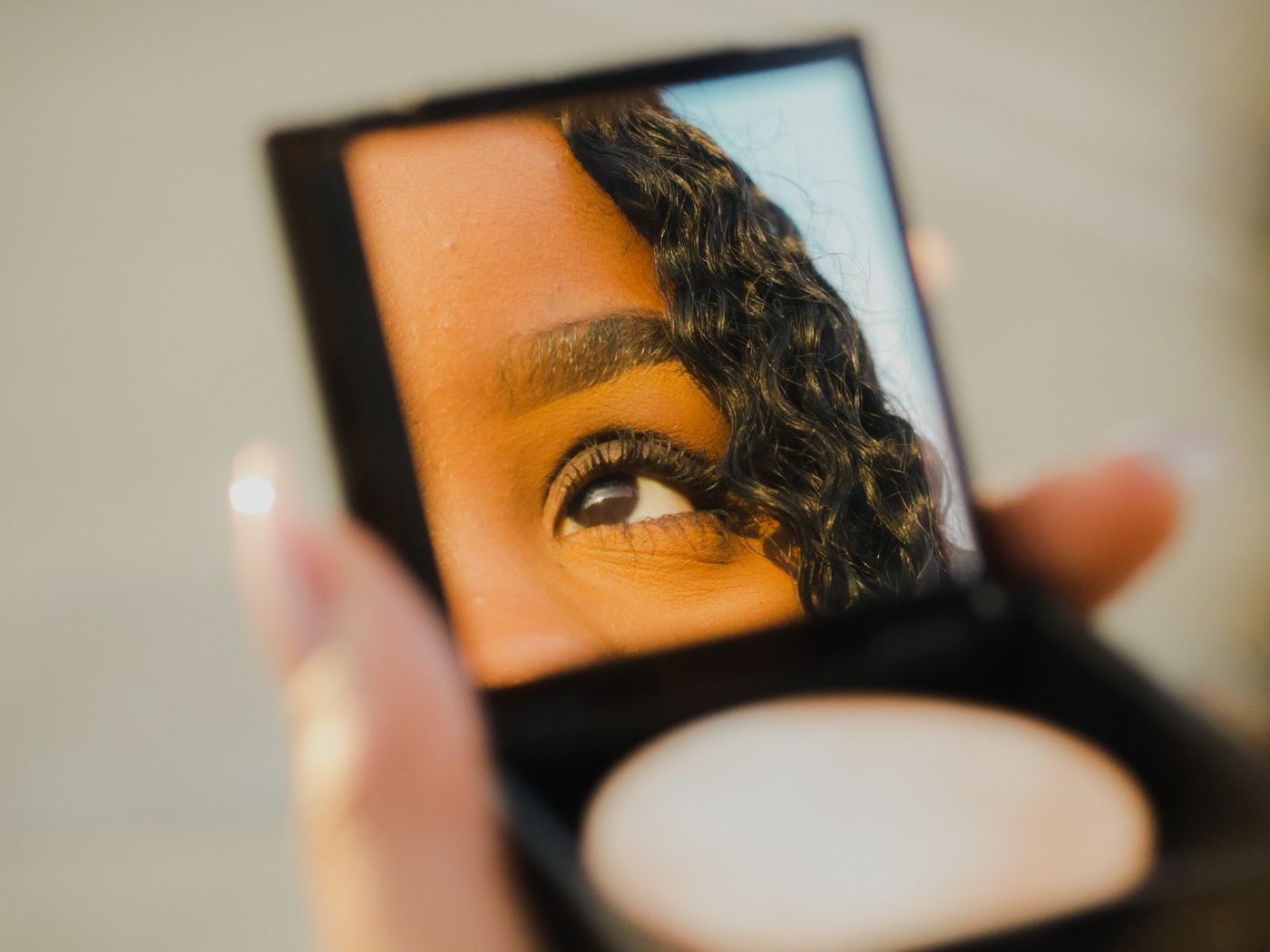 Mirror and foundation compact with woman's eye and brow appearing in the mirror