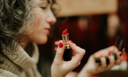 Woman holding a used lipstick while looking into a hand mirror