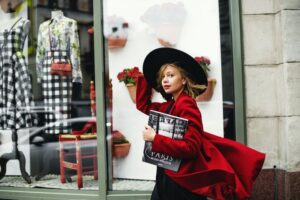 Woman holding her hat while shopping down a street