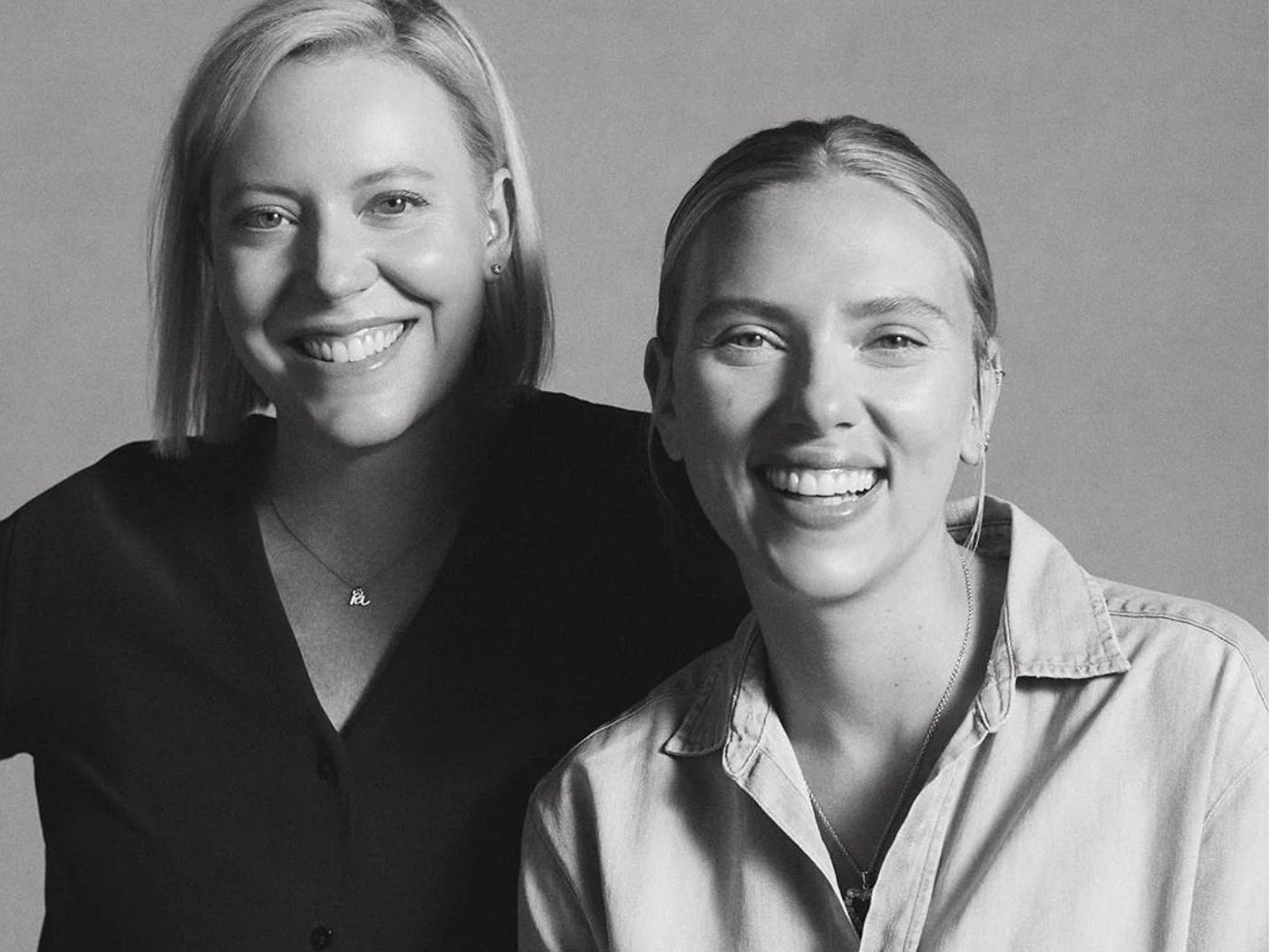 Black and white portrait of two women, one in a black shirt and one in a white shirt, smiling.