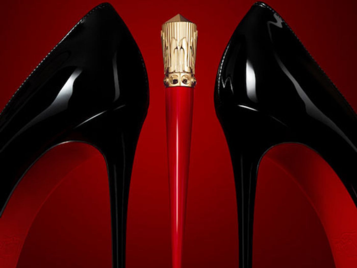 A slim red, stiletto heel-shaped lipstick case positioned between a pair of black Christian Louboutin stilettos with red soles. October Cheat Sheet 2023