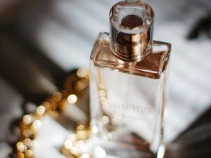 Glass perfume bottle on table with gold necklace.