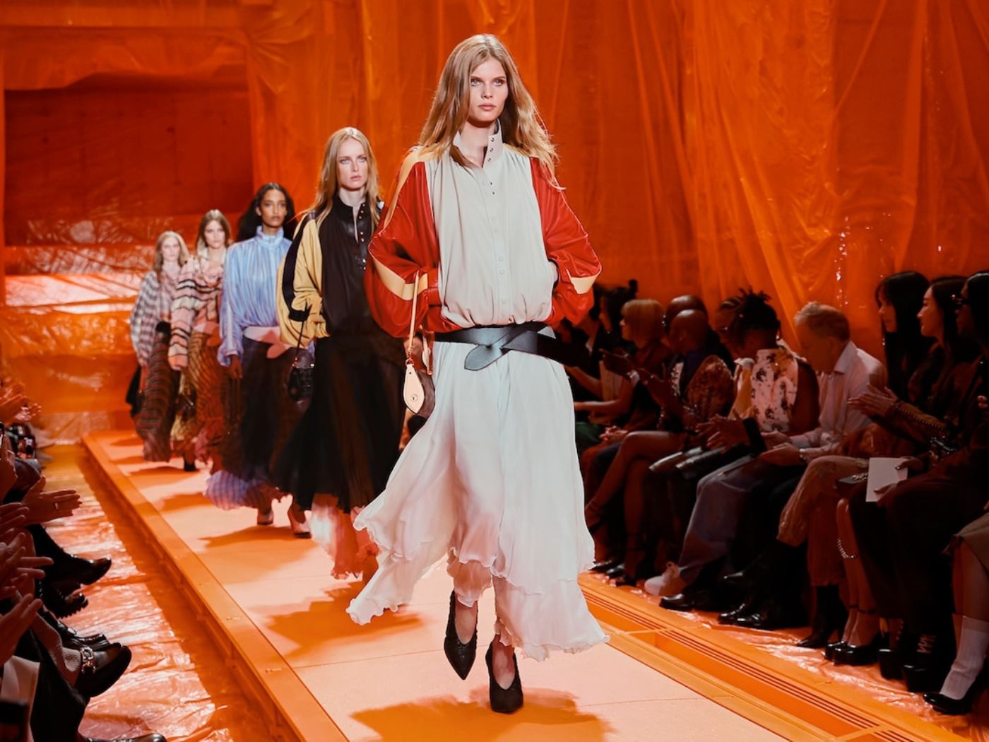 Models walking single file down a runway in flowing spring/summer clothes by Louis Vuitton in Paris.