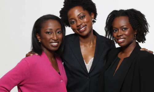 Three women stand together, smiling.