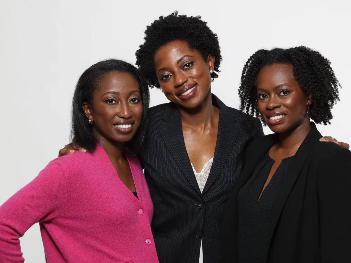Three women stand together, smiling.