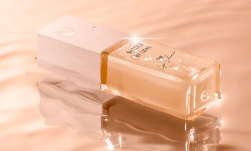 A tube of peach-coloured lip gloss is laid on a matching, rippling surface.
