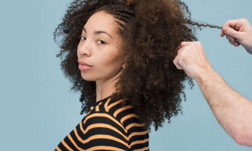 Model with textured hair wearing and orange and black striped t-shirt has her hair styled against a blue background.