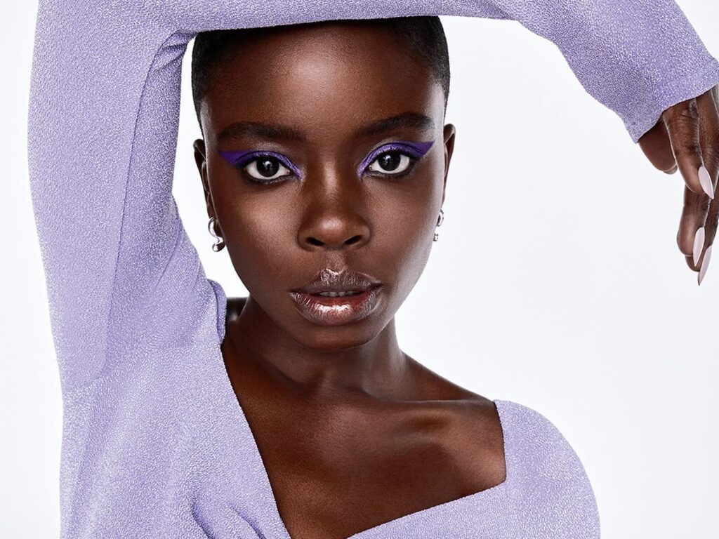 Joy Sunday wearing bright violet eye makeup and a matching top.