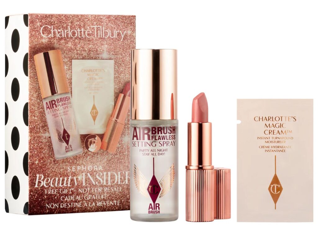 A gold-coloured beauty gift box with three products: an Airbrush Setting Spray in a bottle, A lipstick in a golden case and a sachet with a skincare sample.