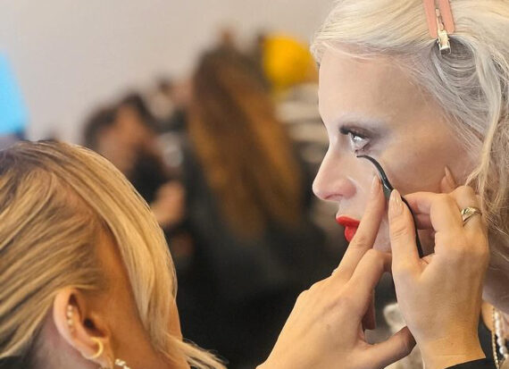 Make-up artist applies lower false lashes to a model backstage at a fashion show.