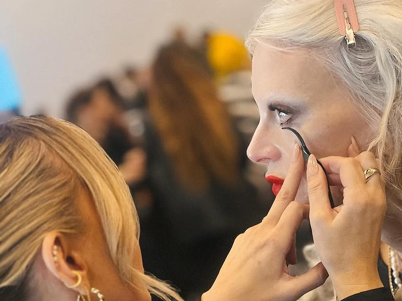 Make-up artist applies lower false lashes to a model backstage at a fashion show.