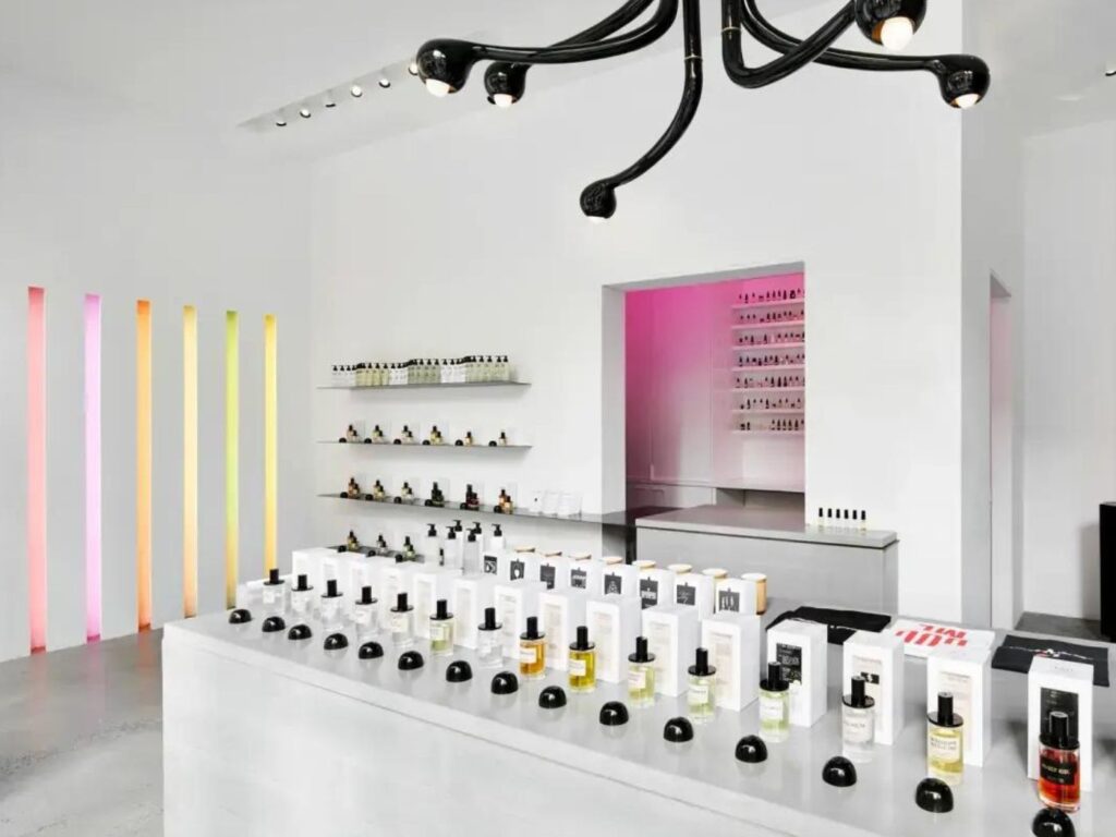 Interior of a perfume shop, with white walls and counters and multi-coloured strip light fittings and simple glass bottles in white boxes on display.