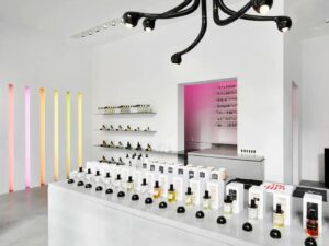 Interior of a perfume shop, with white walls and counters and multi-coloured strip light fittings and simple glass bottles in white boxes on display.