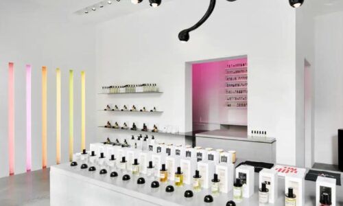 Interior of a perfume shop, with white walls and counters and multi-coloured strip light fittings and simple glass bottles in white boxes on display.