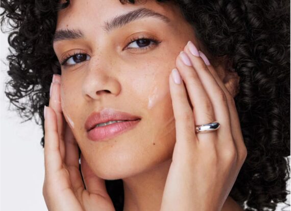 Close-up of a model applying cream to her face with her fingertips.