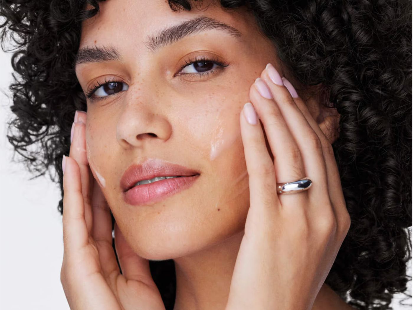 Close-up of a model applying cream to her face with her fingertips.