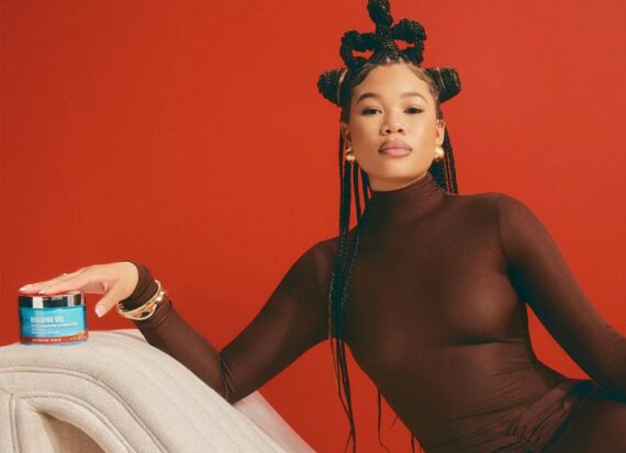 Actress Storm Reid poses on a couch with a tub of Kiss braiding gel.