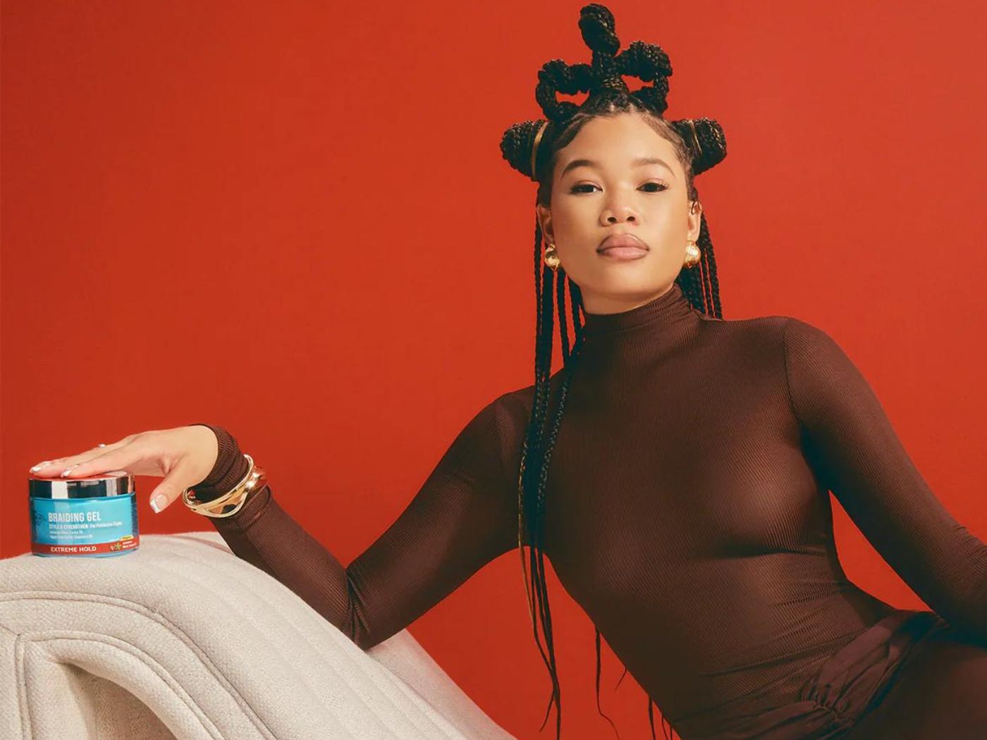Actress Storm Reid poses on a couch with a tub of Kiss braiding gel.
