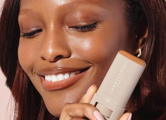 Model holds an Anastasia Beverly Hills Beauty Balm stick against her face.