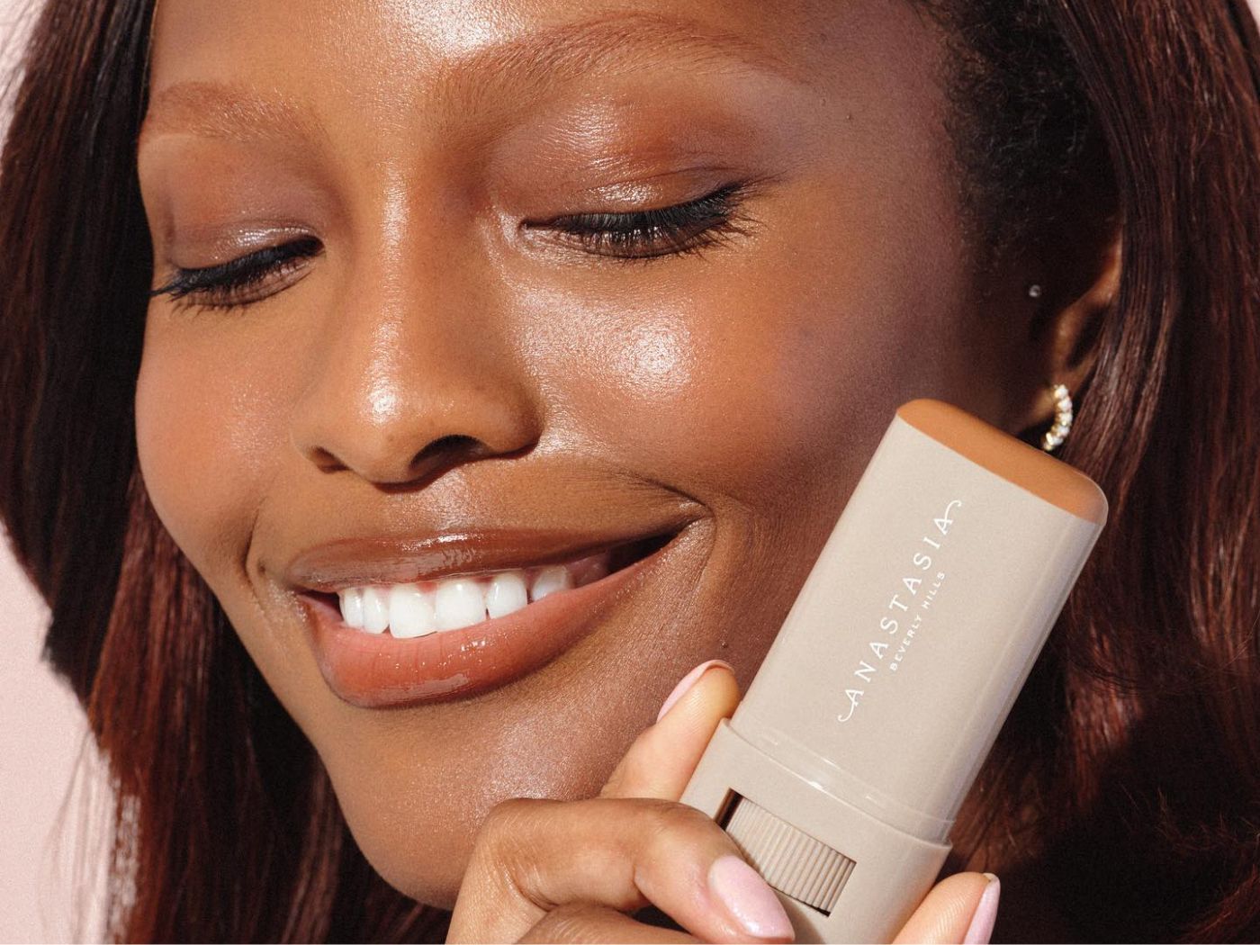 Model holds an Anastasia Beverly Hills Beauty Balm stick against her face.