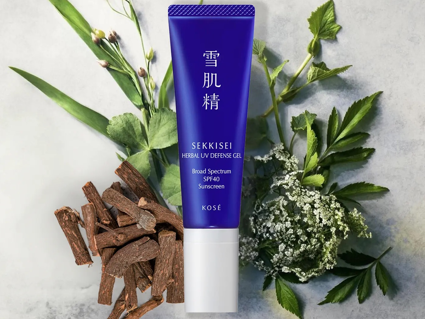 A tube of blue Sekkisei sunscreen placed on top of a selection of natural herbs and extracts.