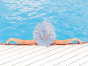 Woman lounging in pool wearing a large blue and white sunhat.