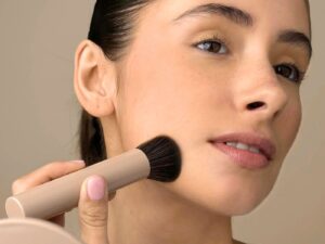 Model applying makeup to cheek using a beige coloured big applicator brush