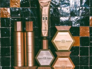 A display of gold and rose gold haircare products against black tiles in a bathroom.