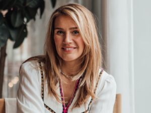 Portrait of NEOM Wellbeing founder Nicola Elliott, wearing a white blouse with multi-coloured collar trim.