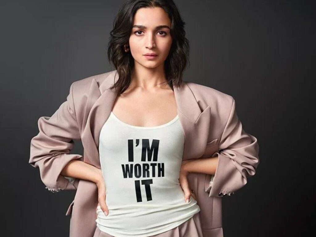 Alia Bhatt wears a pink trouser suit and black and white t-shirt with the slogan "I'M WORTH IT".