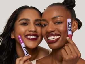 Two girls smiling, holding purple tubes of Kulfi makeup