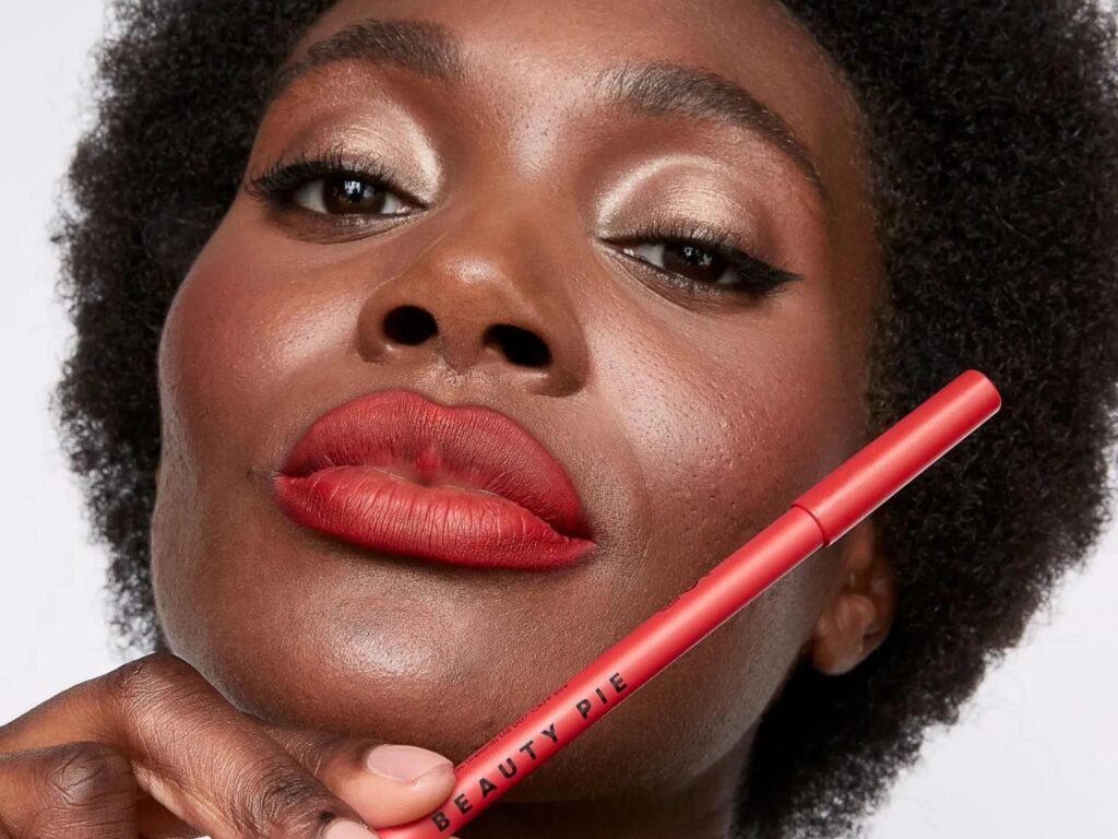 Woman wearing red lipstick, holds a red lip pencil with the words BEAUTY PIE on it.