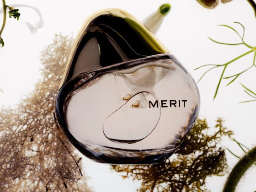 Bottle of fragrance with MERIT label on it, surrounded by botanicals