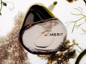 Bottle of fragrance with MERIT label on it, surrounded by botanicals