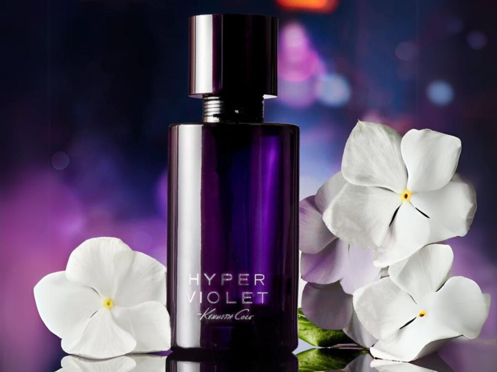 A purple fragrance bottle with the label Hyper Violet sits next to white flowers on a reflective surface