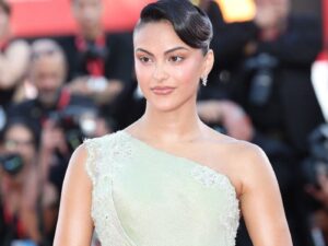 Actress Cmila Mendes on the red carpet wearing an off one shoulder sparkling pale green dress, her hair slicked back and sparkling drop earrings.