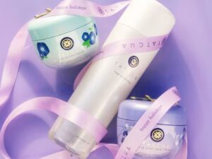 A selection of Tatcha products arranged on lilac satin, with Tatcha logo ribbon swirling around them