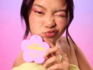 A model against a pink background holding a pink flower shaped cosmetics compact with the words HELLO DAISE on it.