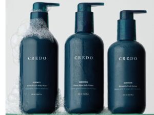 Three marine blue colored bottles of body care products on a shelf, with soap suds around them, with the word CREDO on each